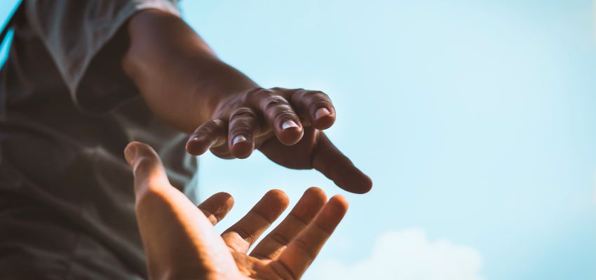 Two open hands reaching toward each other against a bright sky, symbolizing offering help and connection – depicting how should Christians respond to people taking advantage of them through generous love, lending without expecting return, and showing mercy as God does to the ungrateful.