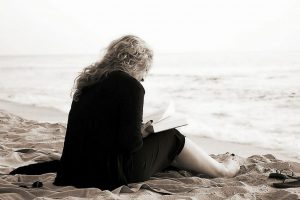 Woman with anxiety reading a book by the beach