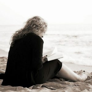 Woman with anxiety reading a book by the beach
