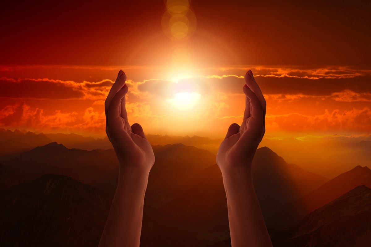 A paid of hands in a worshipping form during sunrise