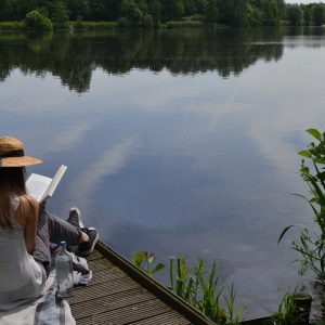 A woman reading a mystery novel by the lake.