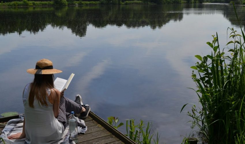 A woman reading a Christian mystery novel by the lake.