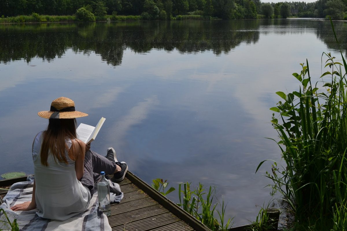 A woman reading a mystery novel by the lake.