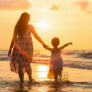 A mother walking with her daughter on the beach.