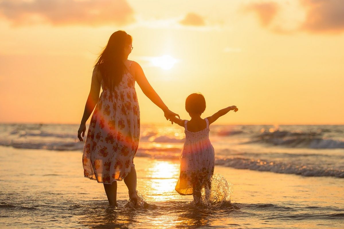 A mother walking with her daughter on the beach.