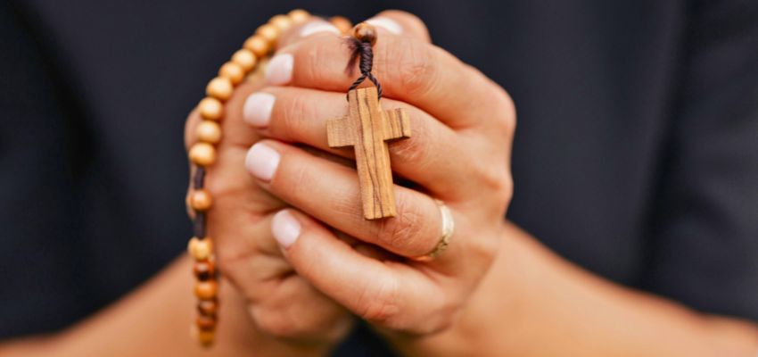 Woman praying the rosary in Latin as she holds the beads in her hands during a quiet moment of reflection.