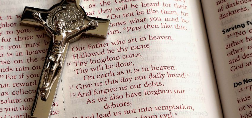 Silver crucifix and rosary placed over a Bible, symbolizing Praying the rosary in Latin as part of a devotional practice.