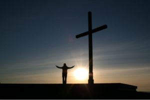 A person with their hands in the air near a crucifix.