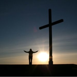 A person with their hands in the air near a crucifix.