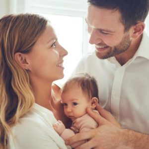 Parents holding their child and smiling at eachother.