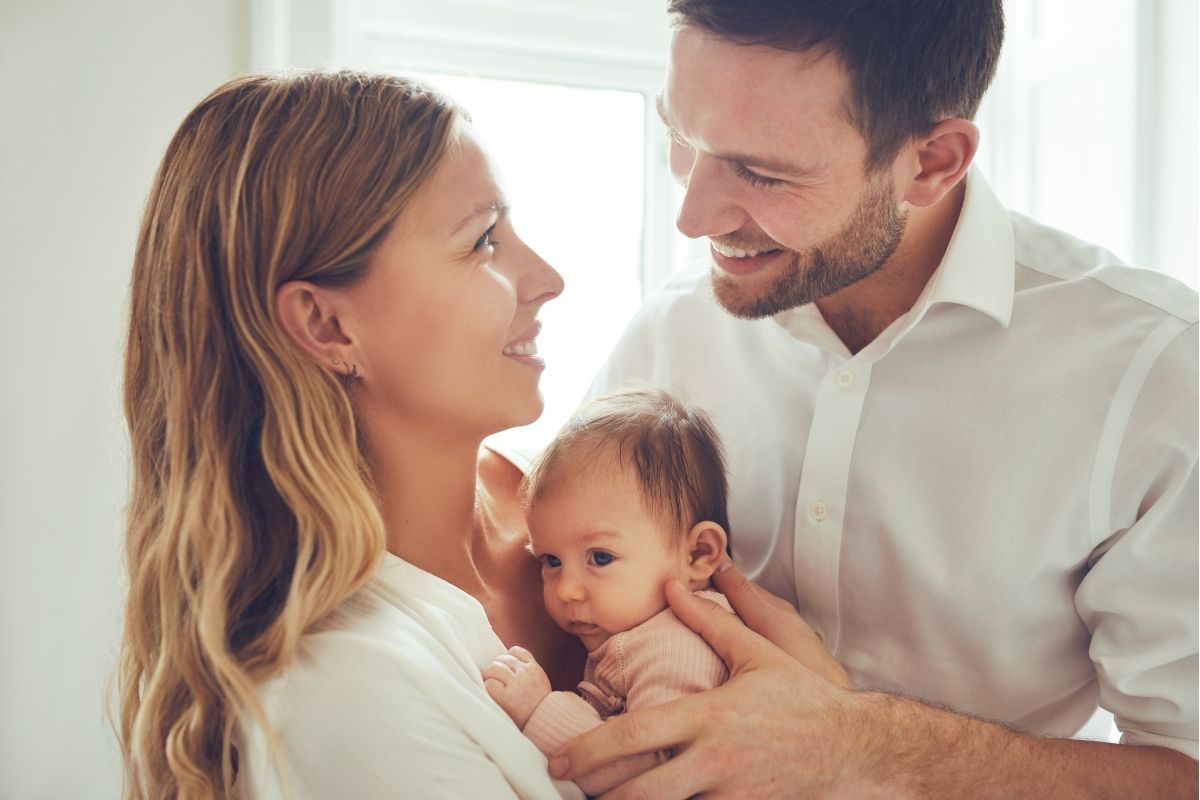 Parents holding their child and smiling at eachother.