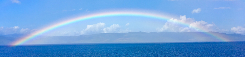 A rainbow under a blue sky and over the ocean.