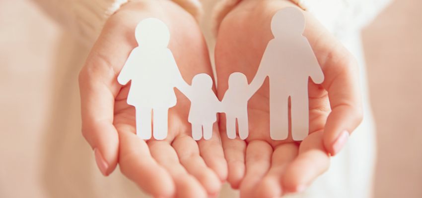 Hands cradling a white paper cutout of a mother, father, and two children, symbolizing the protection and care taught in bible verses about parenting responsibilities.