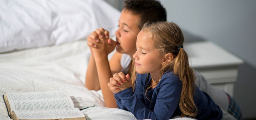 Children reading the Bible and saying night prayers for family together before bed.