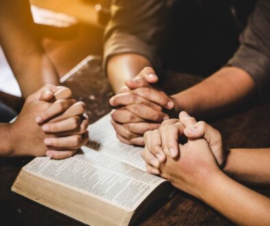 Family holding hands in unity during night prayers for family with an open Bible.