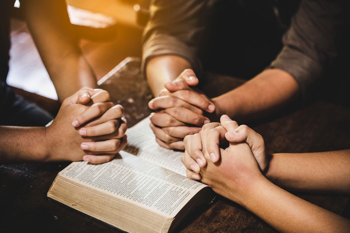 Family holding hands in unity during night prayers for family with an open Bible.