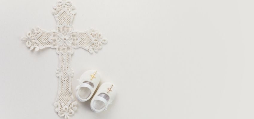 An ivory Catholic cross and white baby shoes on a white background.