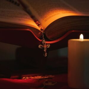 A Catholic prayer candle beside an open bible.