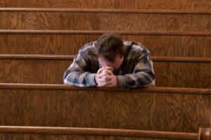 A man praying while kneeling on the church pew.