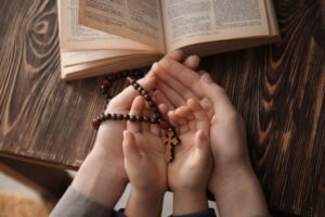 The hands of a good mother and her son holding a rosary while reading the bible show a great character.