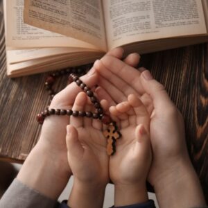 The hands of a good mother and her son holding a rosary while reading the bible show a great character.