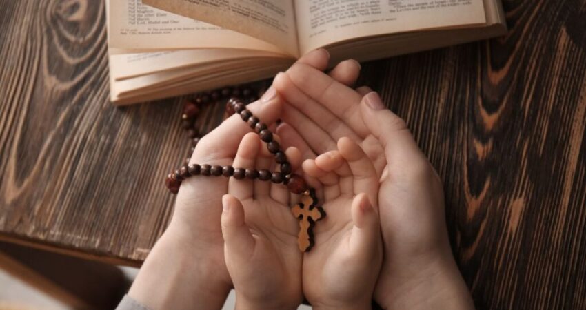 The hands of a good mother and her son holding a rosary while reading the bible show a great character.