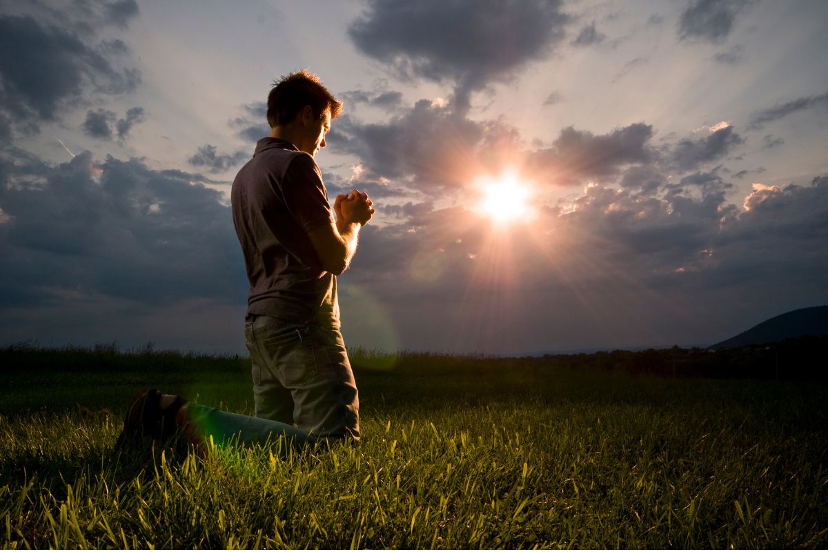 A man knelt on the grass to pray for a miracle to God.