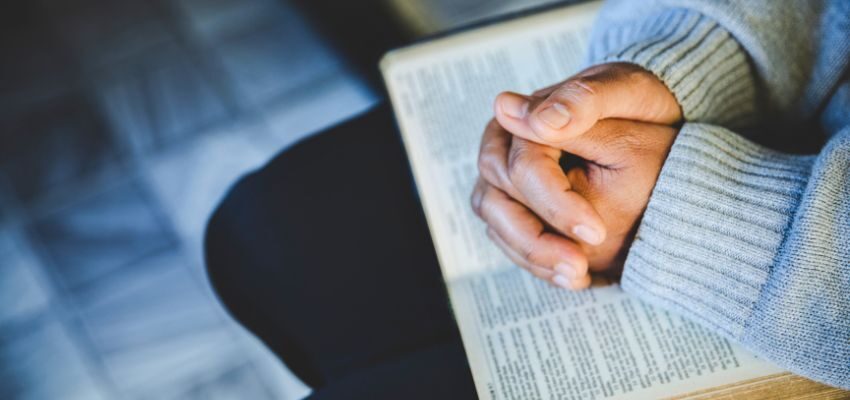 Close-up of folded hands in Catholic birthday prayer with soft light.
