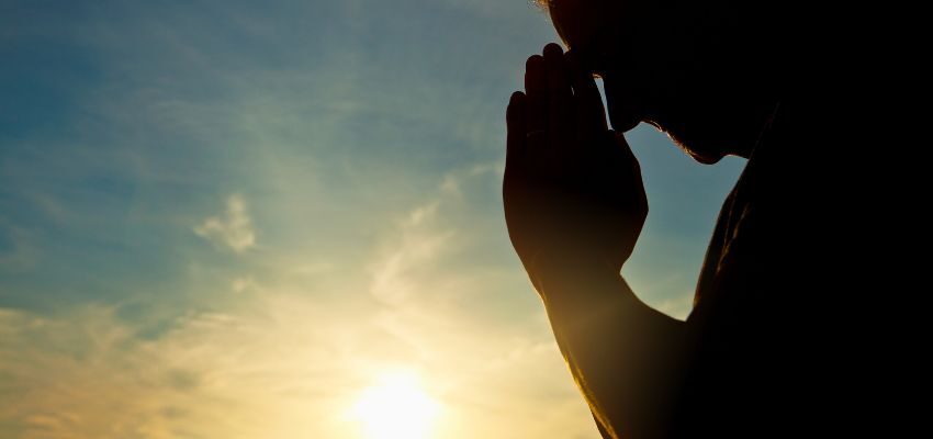 A man in Catholic birthday prayer under the rising sun.