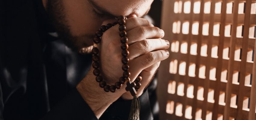 Man in deep prayer holding a rosary, contemplating mortal sin and faith.