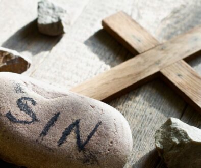 Stone inscribed with 'SIN' beside a wooden cross, symbolizing the idea of mortal sin.