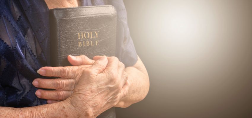 Elderly person holding a Holy Bible close, reflecting on the concept of mortal sin.