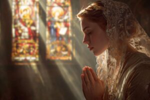 Catholic woman praying with a chapel veil inside a church illuminated by stained glass light, showing why Catholics wear chapel veils as an expression of reverence.