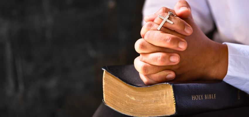 Hands folded in prayer over a Bible while offering prayers before the blessed sacrament.