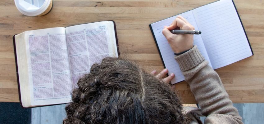 The person is taking notes while reading the bible.