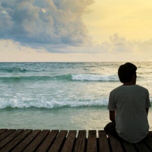 The man sitting in front of the sea feels alone.