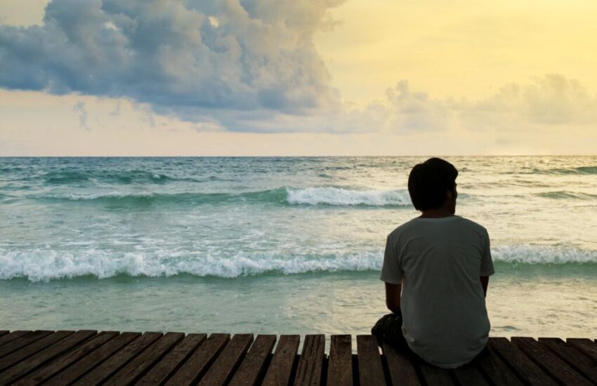 The man sitting in front of the sea feels alone.