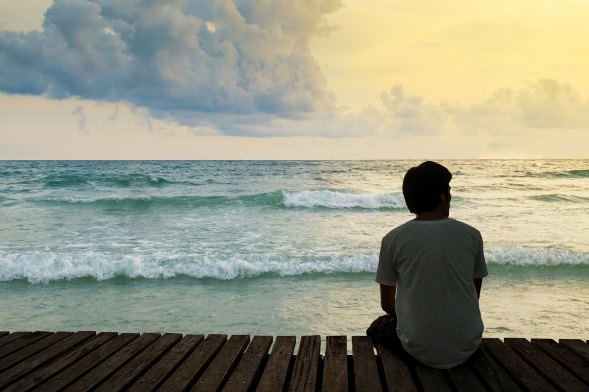 The man sitting in front of the sea feels alone.