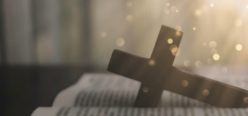 Wooden cross resting on an open Bible with soft glowing light, evoking catholic prayers for protection and faith.