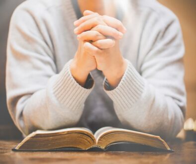 Person with hands clasped in prayer over an open holy book, representing moments of catholic prayers for protection.