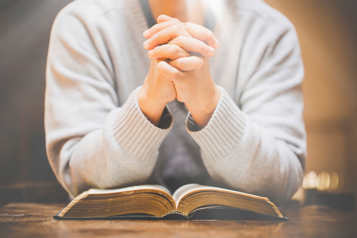 Person with hands clasped in prayer over an open holy book, representing moments of catholic prayers for protection.