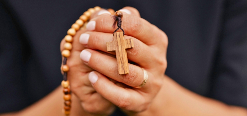 Hands gently holding a wooden rosary and cross, a common symbol used during catholic prayers for protection.