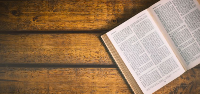 Open Holy Bible displaying short bible verses on a rustic wooden surface