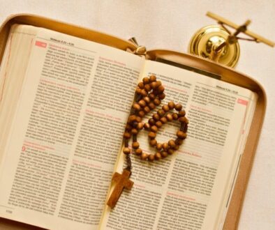 Open Bible with rosary beads resting on short bible verses pages