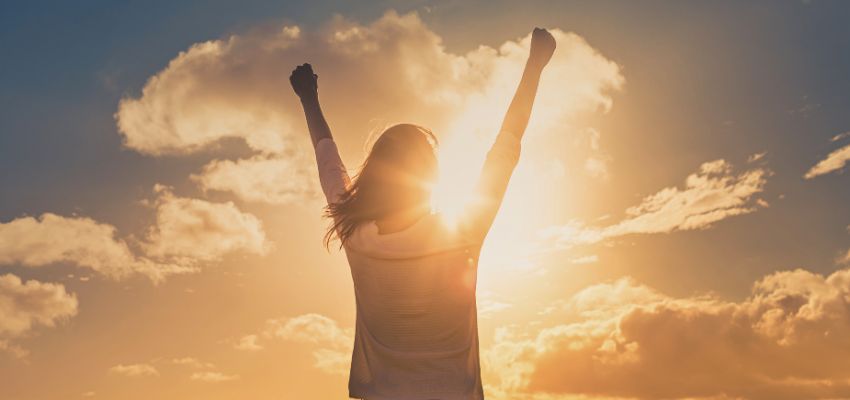 Woman raising her arms toward the sunrise, symbolizing hope and renewal inspired by bible verses about disappointment.