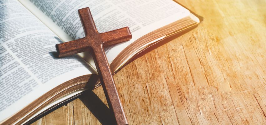Wooden cross resting on the open pages of a Bible with warm sunlight, symbolizing faith and scripture – representing bible verses about community that emphasize unity in Christ, fellowship, and love among believers.