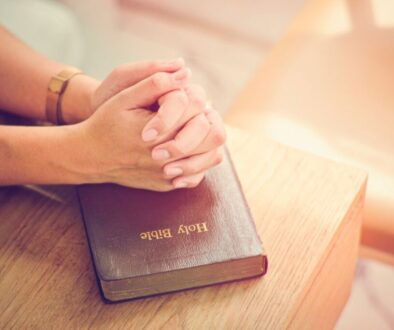 Person praying with hands clasped over a Holy Bible, reflecting on biblical principles and spiritual guidance.