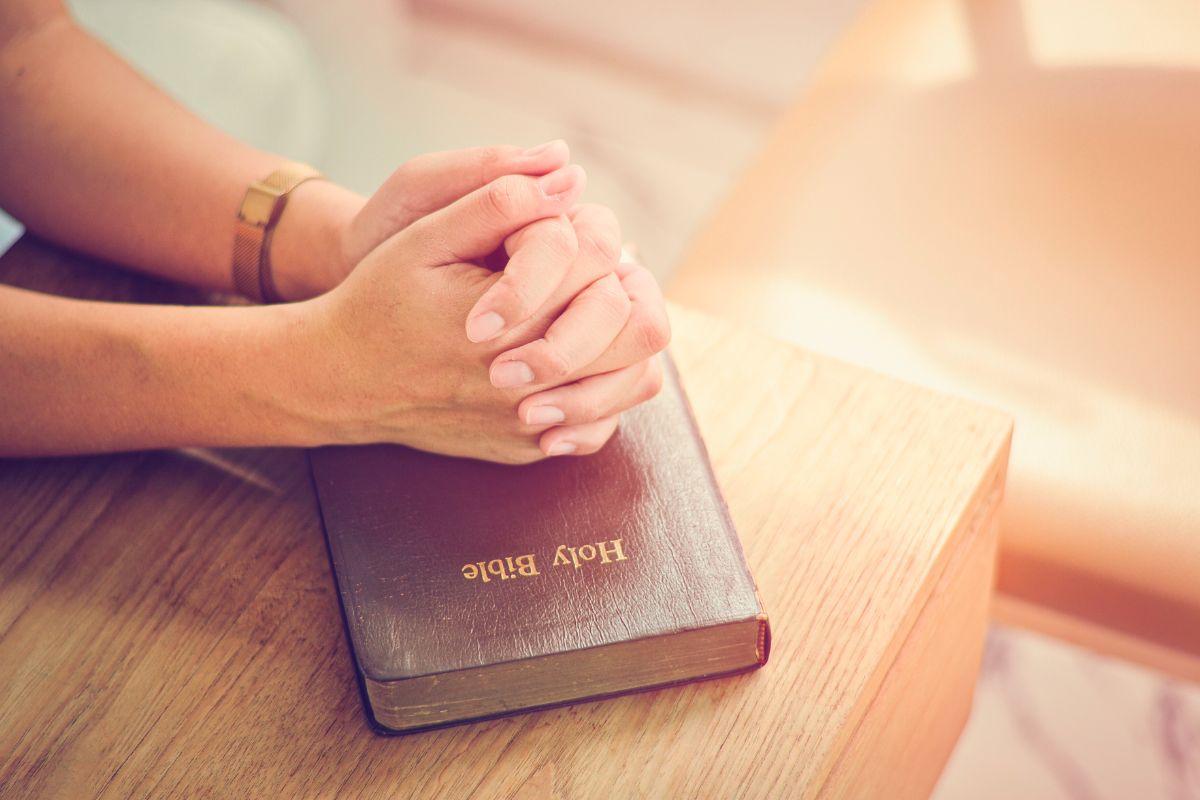 Person praying with hands clasped over a Holy Bible, reflecting on biblical principles and spiritual guidance.