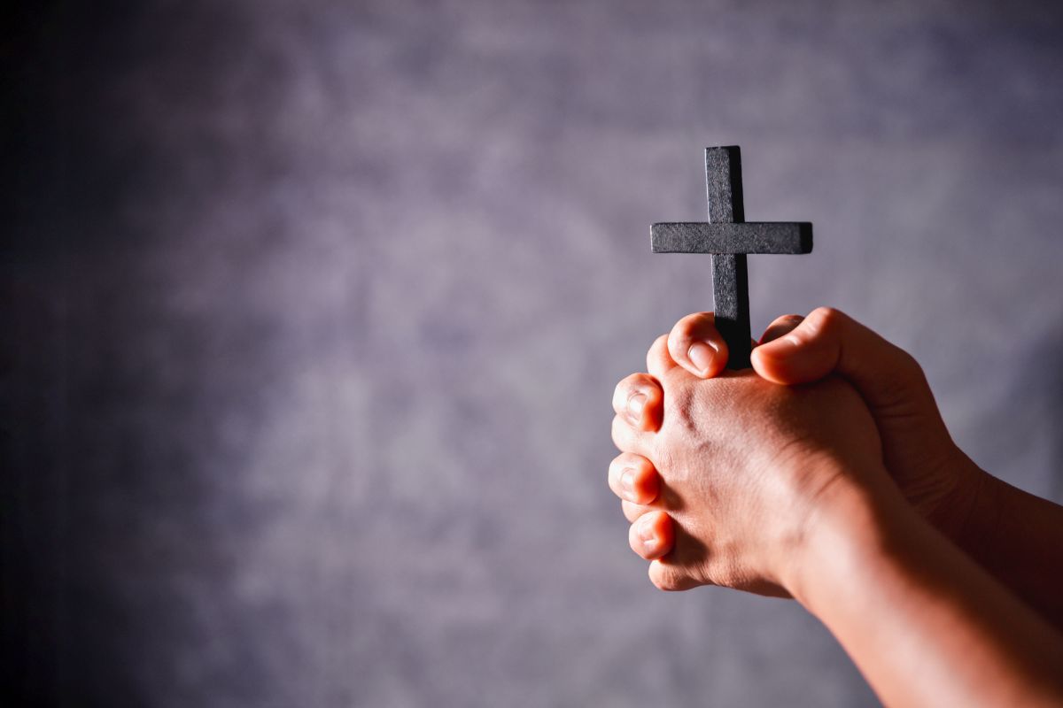 A man holds a wooden cross while praying.