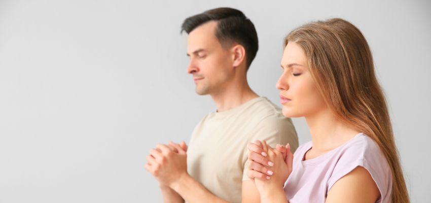 Prayer for husband and wife: A man and woman sitting together with eyes closed and hands clasped in prayer, showing a moment of spiritual unity.